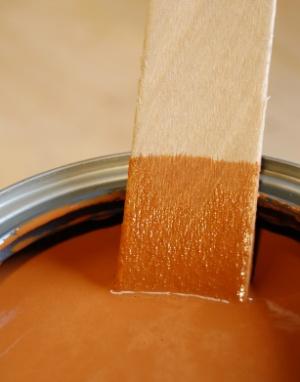 Wooden mixing stick partially submerged in new can cinnamon tinted wood stain.